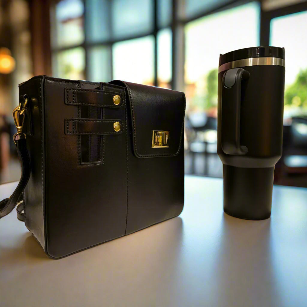 Black leather bag with gold accents next to a black travel mug on a table with a patterned wall in the background.